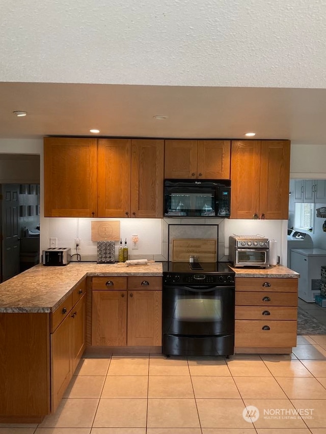 kitchen with light tile patterned flooring, black appliances, a textured ceiling, and washer / dryer