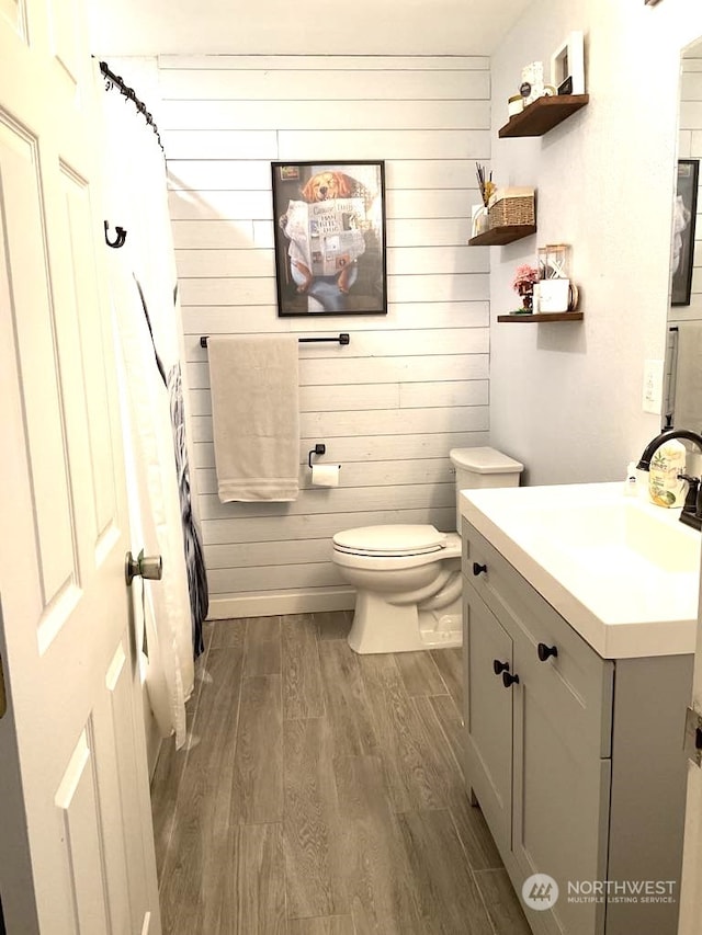 bathroom featuring hardwood / wood-style floors, vanity, wood walls, and toilet