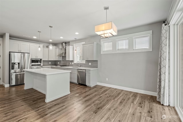 kitchen with appliances with stainless steel finishes, a center island, wall chimney range hood, and pendant lighting