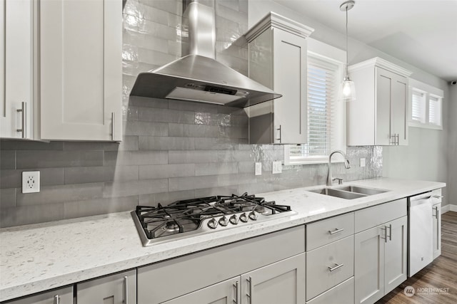 kitchen with appliances with stainless steel finishes, decorative backsplash, sink, wall chimney range hood, and decorative light fixtures