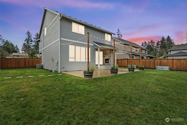 back house at dusk with a patio area, a fireplace, central AC unit, and a yard