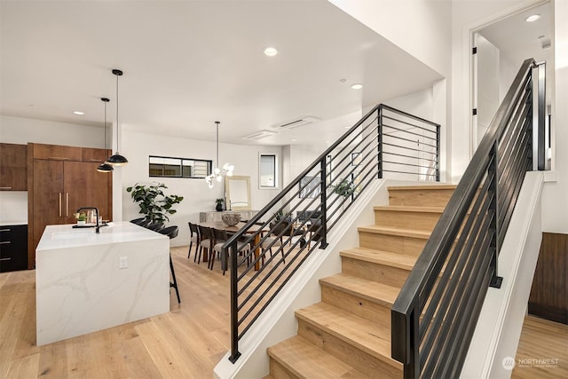 staircase with sink, wood-type flooring, and an inviting chandelier