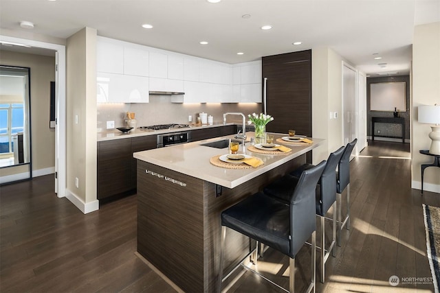 kitchen with sink, a kitchen bar, dark brown cabinets, stainless steel appliances, and a center island with sink