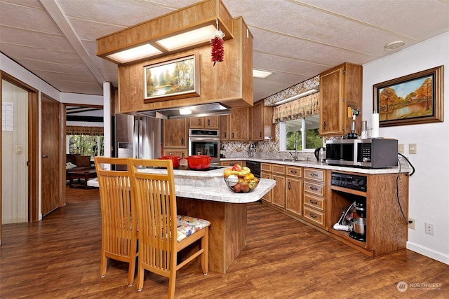 kitchen with dark hardwood / wood-style flooring, stainless steel appliances, a kitchen bar, and kitchen peninsula