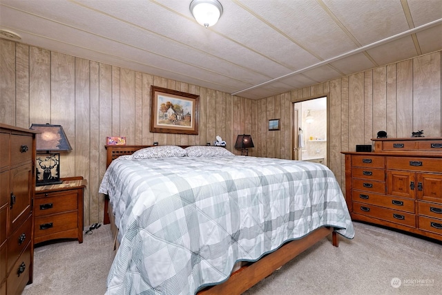 bedroom with light carpet, ensuite bath, and wood walls