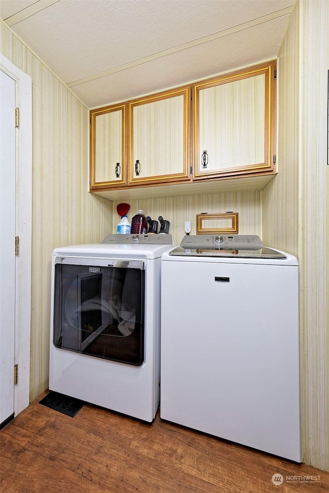 washroom with hardwood / wood-style floors, washer and clothes dryer, cabinets, and wood walls