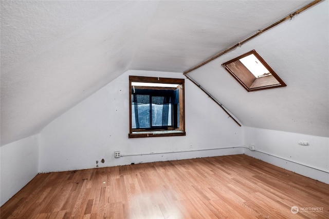 bonus room with lofted ceiling with skylight, a textured ceiling, and hardwood / wood-style flooring