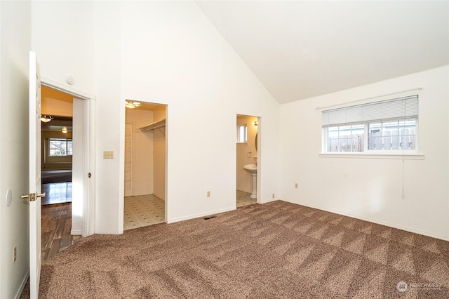 unfurnished bedroom featuring a walk in closet, multiple windows, connected bathroom, and high vaulted ceiling