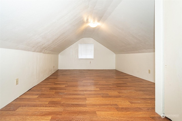 additional living space with lofted ceiling, a textured ceiling, and hardwood / wood-style floors