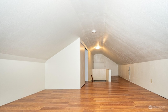 additional living space featuring light wood-type flooring, vaulted ceiling, and a textured ceiling