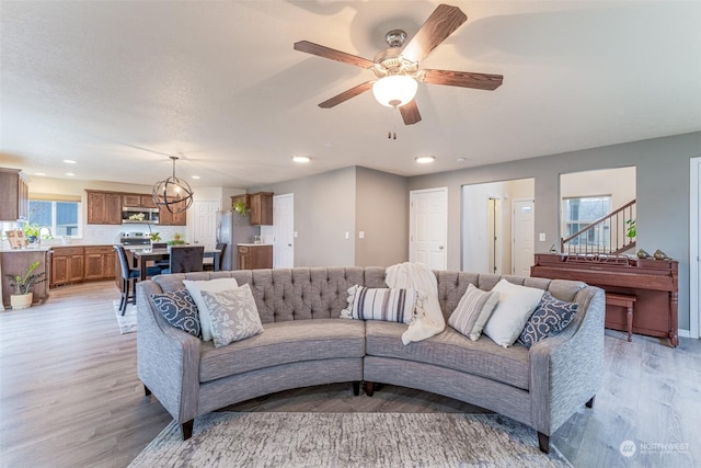 living room featuring light wood-type flooring, ceiling fan with notable chandelier, and sink