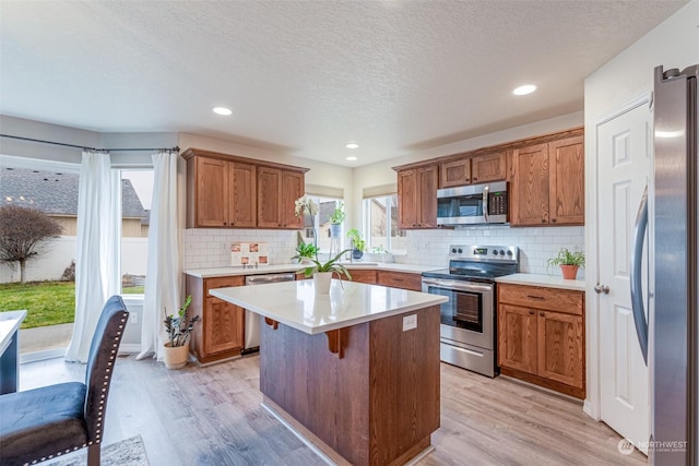 kitchen with appliances with stainless steel finishes, light wood-type flooring, a textured ceiling, and a kitchen island