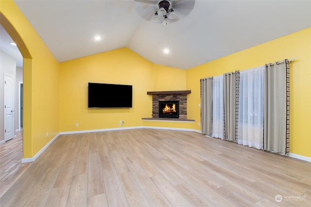 unfurnished living room with ceiling fan, lofted ceiling, light hardwood / wood-style flooring, and a stone fireplace