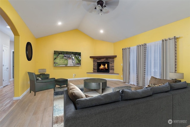 living room with light wood-type flooring, ceiling fan, lofted ceiling, and a stone fireplace