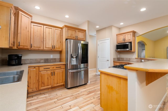 kitchen featuring a breakfast bar, kitchen peninsula, sink, light hardwood / wood-style flooring, and stainless steel appliances