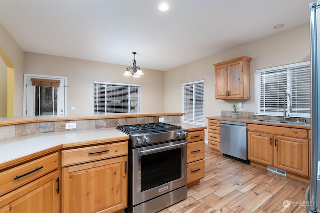 kitchen featuring pendant lighting, stainless steel appliances, sink, a notable chandelier, and light wood-type flooring