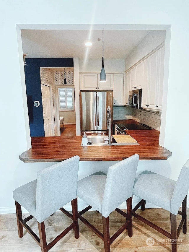 kitchen featuring pendant lighting, white cabinets, decorative backsplash, kitchen peninsula, and stainless steel appliances