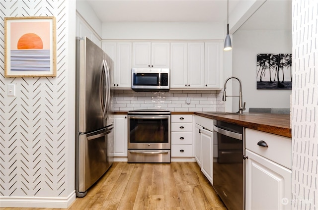 kitchen with butcher block counters, sink, white cabinetry, decorative light fixtures, and stainless steel appliances