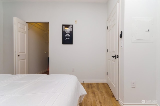 bedroom featuring a walk in closet, light hardwood / wood-style floors, a closet, and electric panel