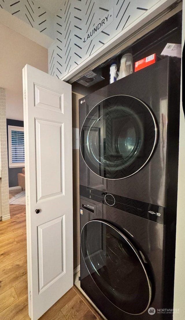 clothes washing area featuring hardwood / wood-style floors and stacked washing maching and dryer