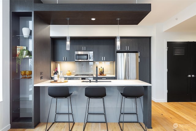 kitchen featuring kitchen peninsula, stainless steel appliances, a kitchen bar, and hanging light fixtures