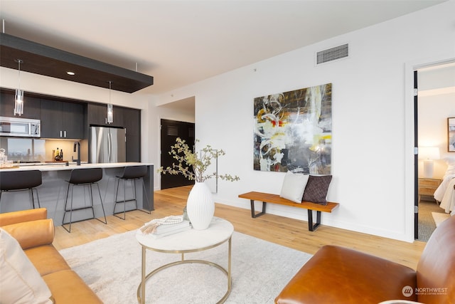 living room with sink, light wood-type flooring, and beamed ceiling