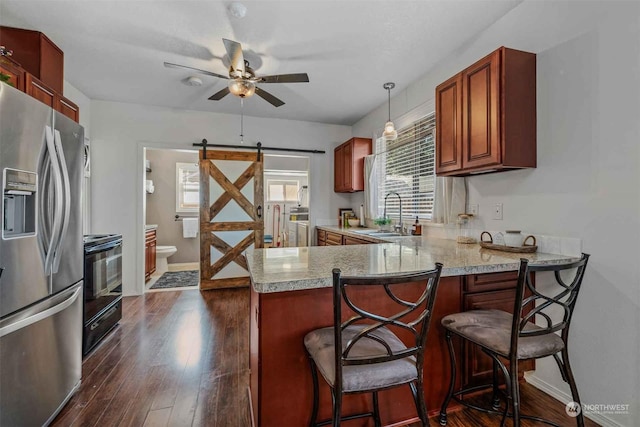 kitchen with kitchen peninsula, stainless steel fridge, a breakfast bar, a barn door, and sink