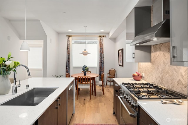 kitchen with appliances with stainless steel finishes, pendant lighting, light stone counters, sink, and wall chimney range hood