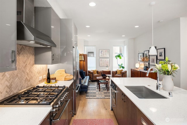 kitchen featuring light stone counters, wall chimney exhaust hood, sink, dark brown cabinets, and decorative light fixtures