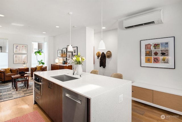 kitchen featuring sink, dishwasher, an AC wall unit, an island with sink, and hanging light fixtures