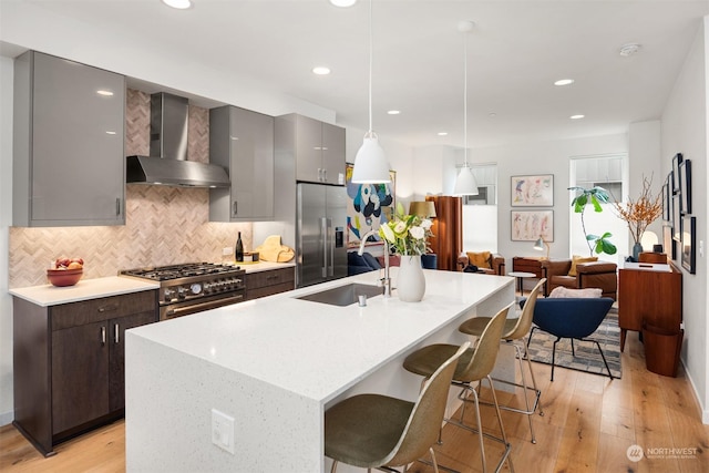 kitchen featuring hanging light fixtures, premium appliances, a center island with sink, wall chimney range hood, and a kitchen bar