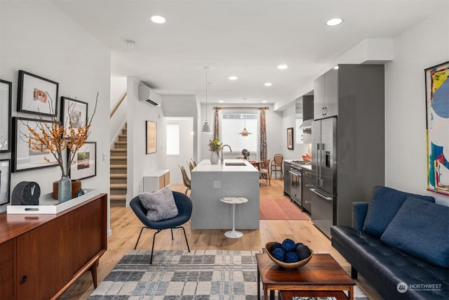 living room featuring a wall mounted AC, light hardwood / wood-style floors, and sink