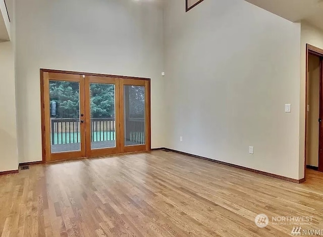 empty room with french doors, a high ceiling, and light wood-type flooring