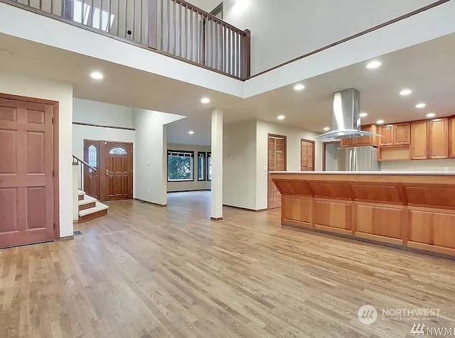 kitchen featuring light hardwood / wood-style floors, island exhaust hood, stainless steel refrigerator, and a high ceiling