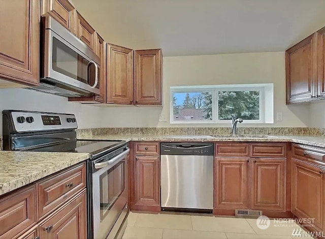 kitchen with light stone countertops, light tile patterned floors, stainless steel appliances, and sink