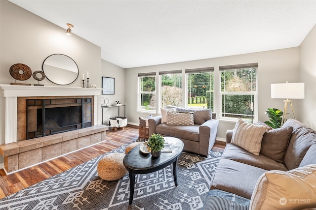 living room featuring a tile fireplace, vaulted ceiling, and hardwood / wood-style flooring