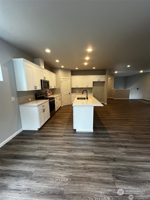 kitchen with stainless steel appliances, dark wood-type flooring, sink, a center island with sink, and white cabinets