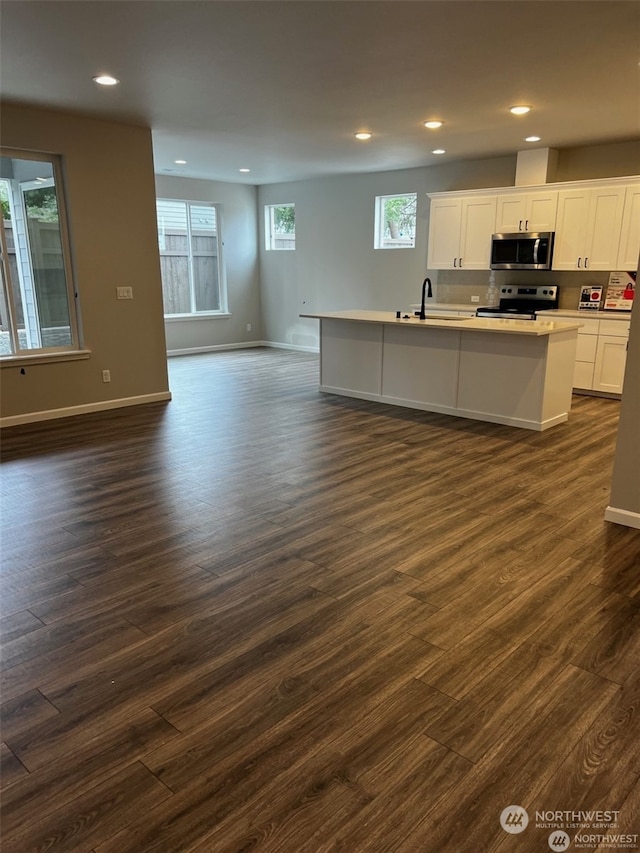 kitchen with dark hardwood / wood-style flooring, stainless steel appliances, sink, a center island with sink, and white cabinets