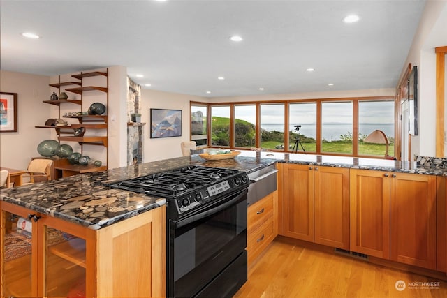 kitchen featuring black range with gas stovetop, kitchen peninsula, dark stone counters, and light hardwood / wood-style flooring