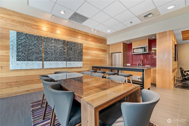 tiled dining room featuring sink, wooden walls, and track lighting