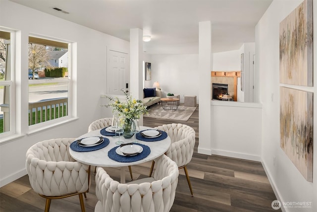 dining area featuring dark wood-type flooring, a fireplace, and baseboards