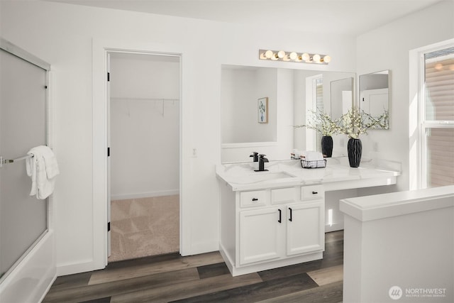 bathroom featuring bath / shower combo with glass door, a walk in closet, wood finished floors, and vanity