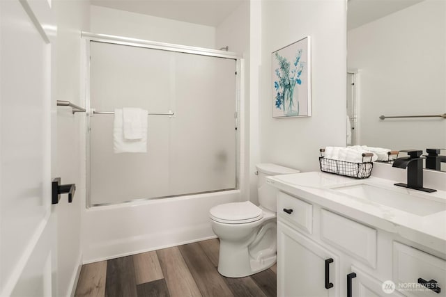 full bathroom featuring toilet, bath / shower combo with glass door, wood finished floors, and vanity