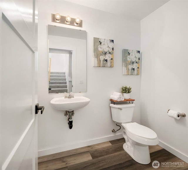 half bath featuring wood finished floors, toilet, and baseboards