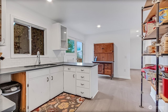 kitchen with backsplash, sink, light wood-type flooring, white cabinetry, and kitchen peninsula