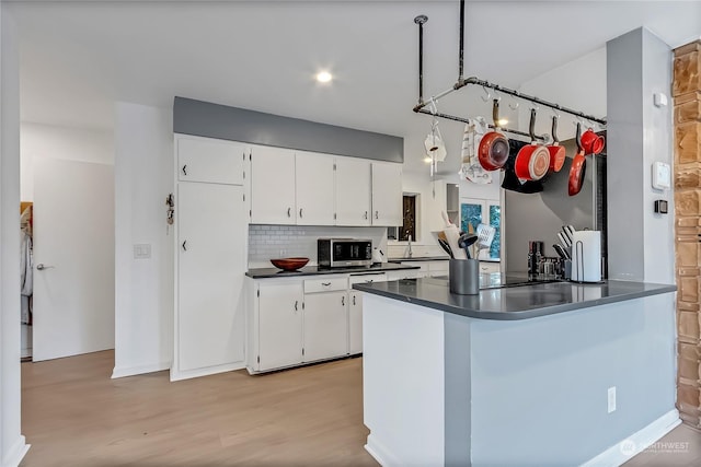 kitchen with kitchen peninsula, backsplash, light hardwood / wood-style flooring, and white cabinetry