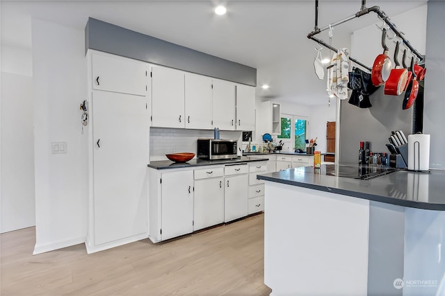 kitchen with black electric stovetop, light wood-type flooring, tasteful backsplash, white cabinets, and hanging light fixtures