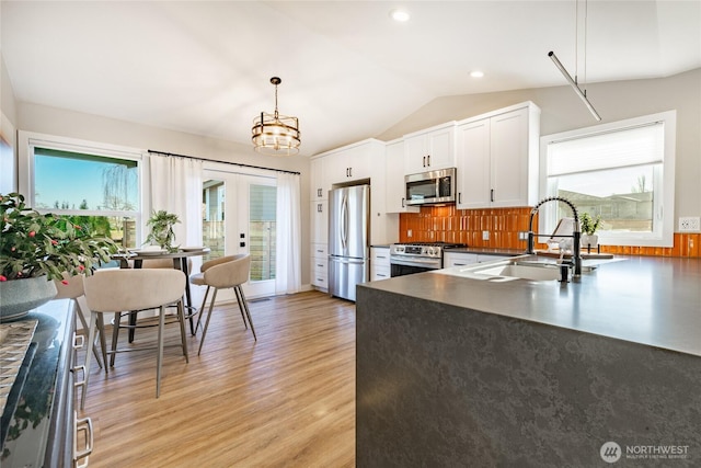 kitchen featuring light wood-style flooring, stainless steel appliances, a sink, vaulted ceiling, and dark countertops