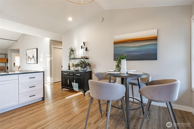 dining area featuring lofted ceiling, light wood finished floors, and baseboards