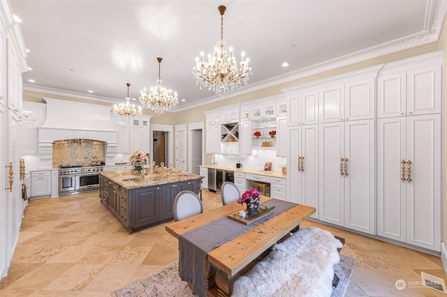 kitchen featuring an island with sink, double oven range, light stone counters, decorative backsplash, and white cabinetry